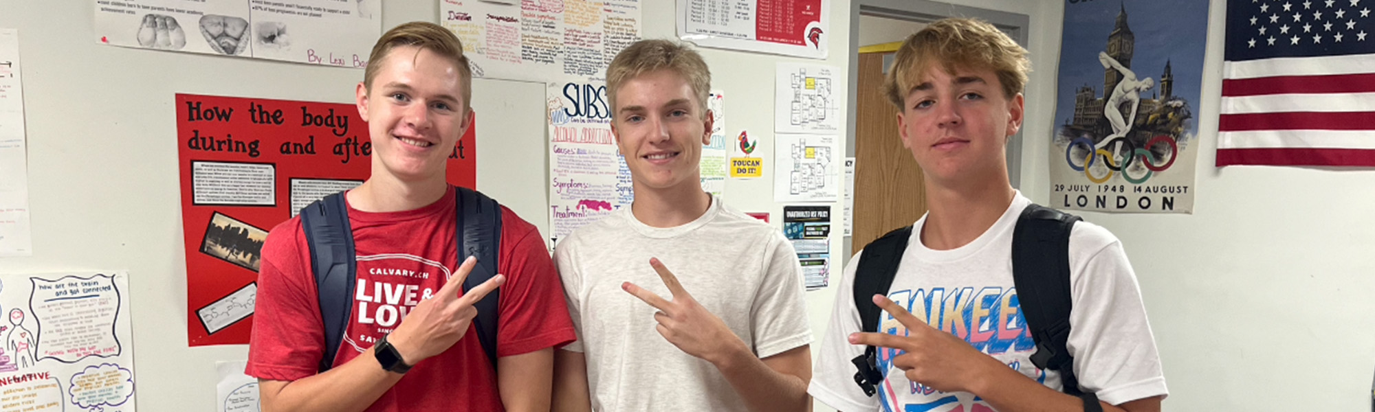 Three students holding fingers in peace signs